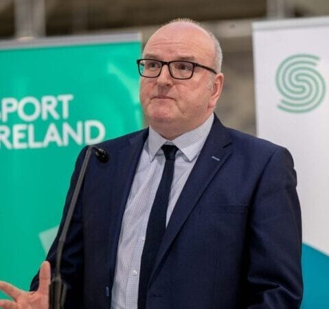 A man in a suit and tie speaks at a podium in front of a Sport Ireland banner.